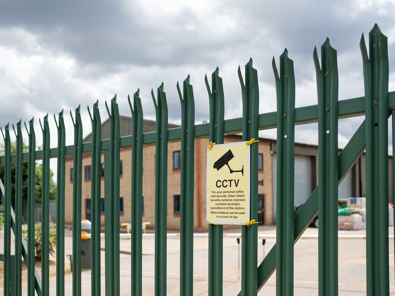 Green pallside steel fencing with cctv sign attached and soft focus background.