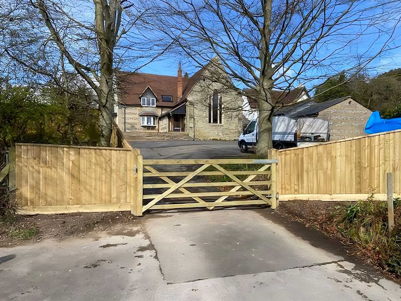 Five bar gate at the end of a driveway with closeboard fencing either side.