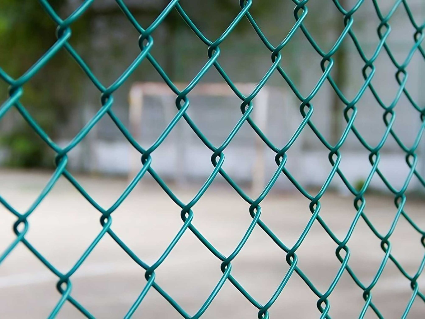 Close up of green chainlink fence with soft focus playground in background.