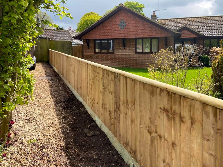 Small closeboard fence along the side of a garden with property in background.