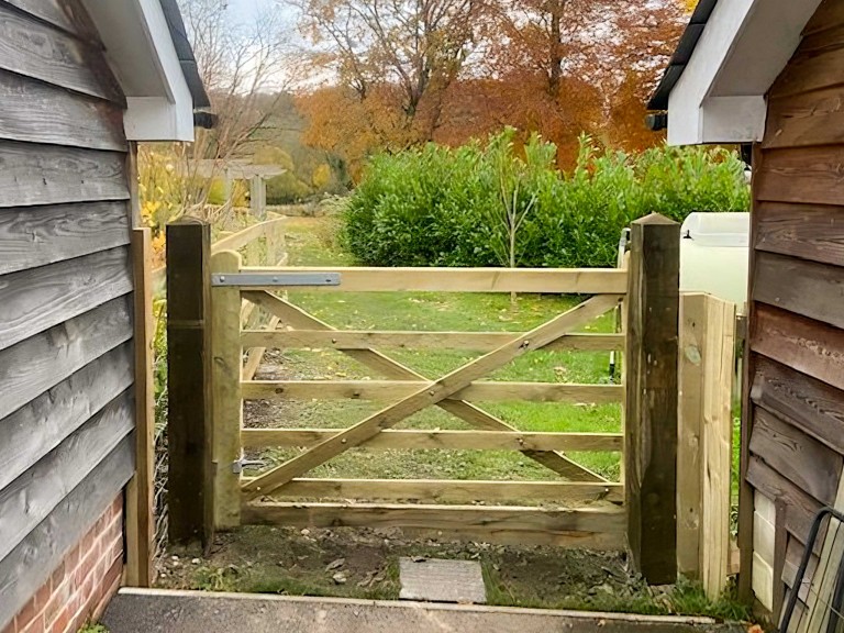 Wooden bridal gate between two buildings looking out onto field.