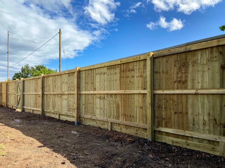 Closeboard fence with vertical boards with bright blue sky in background.
