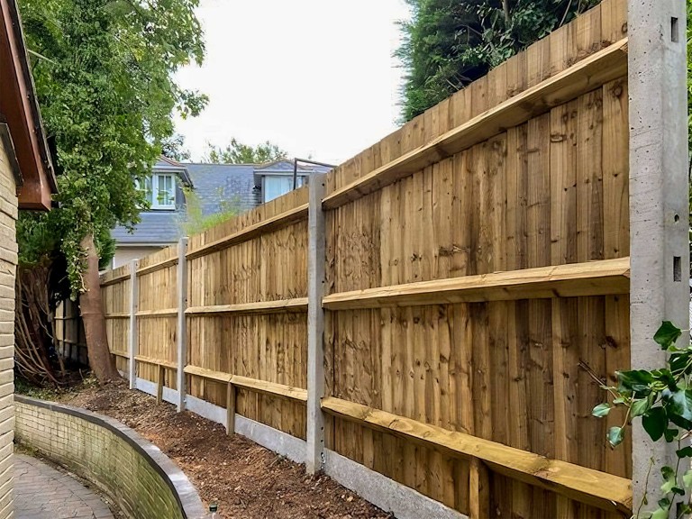 Closebaord fence with concrete bottom and post looking from inside a garden.