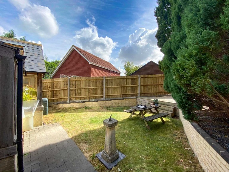 New fencing installed in background of large garden with table and water feature.