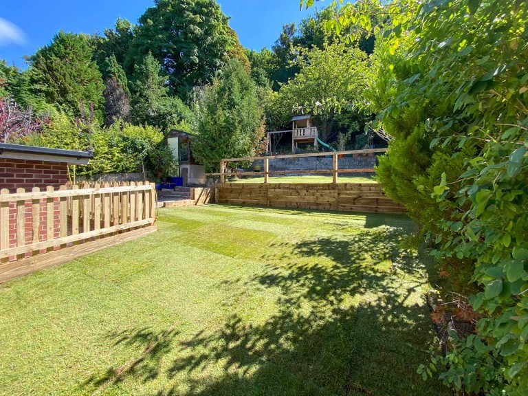 Picket fence in garden with open grass and tree house in background.