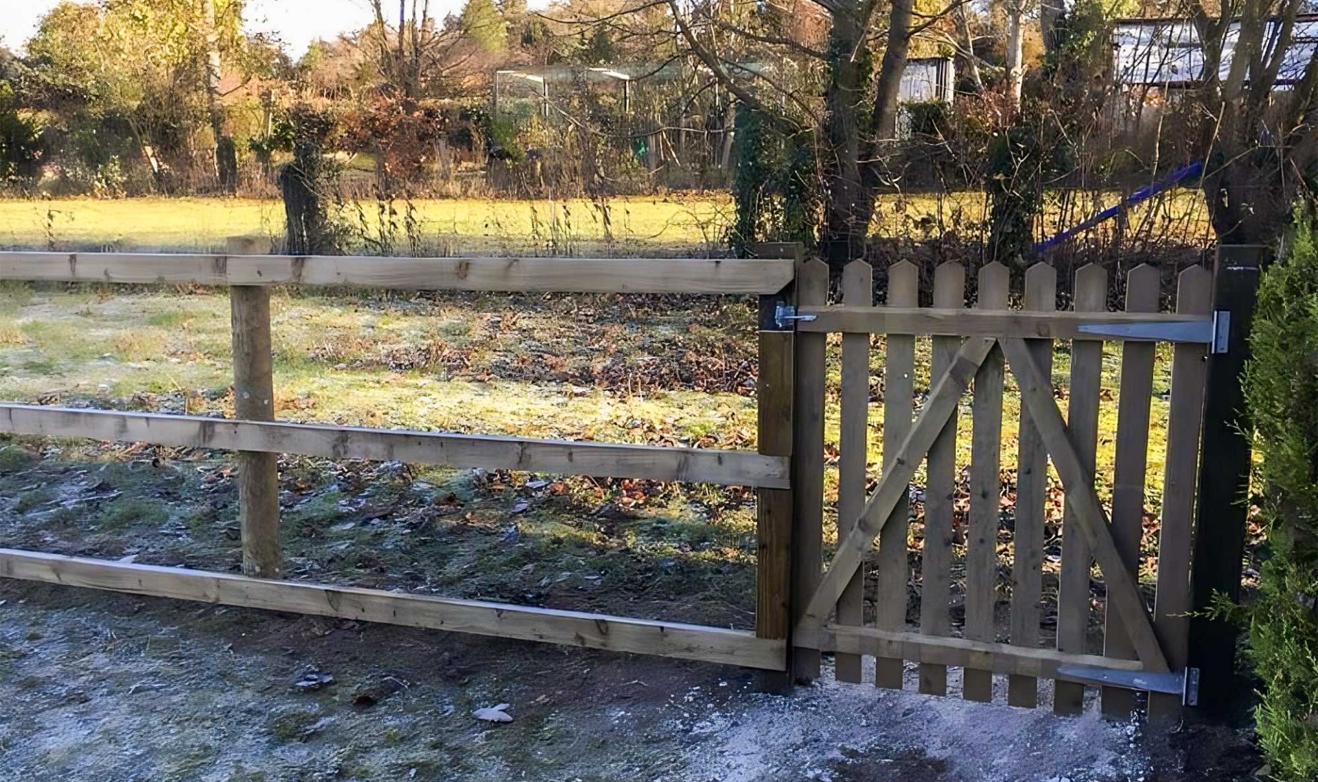 Small picket fence in countryside with wooden fencing to the left.