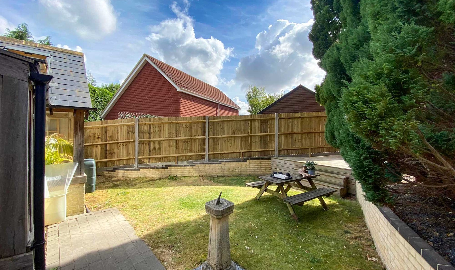 New fencing installed in background of large garden with table and water feature.