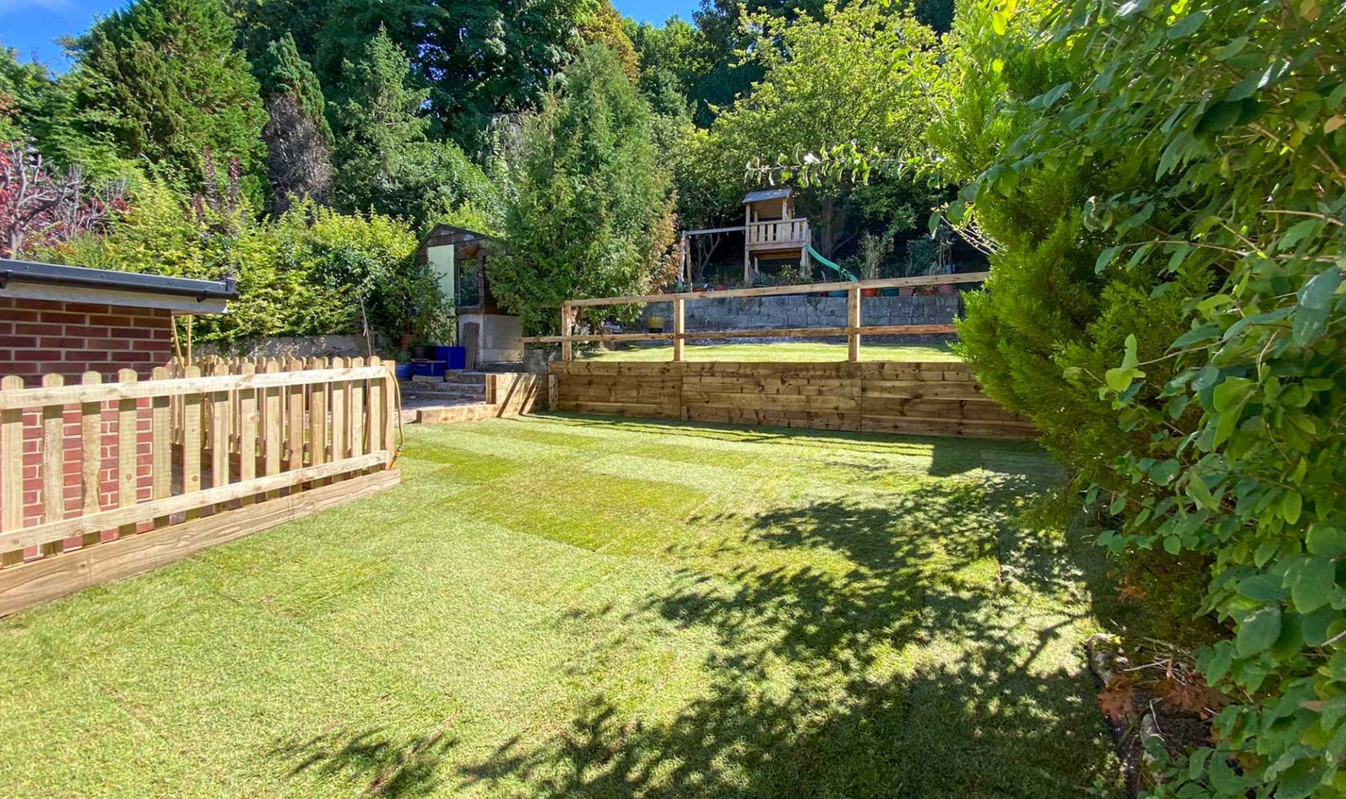 Picket fence in garden with open grass and tree house in background.